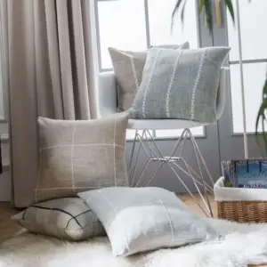 Mehrere beige und graue Kissen mit feinem Linienmuster auf und neben einem Stuhl