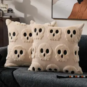 00-21 Zwei cremefarbene Kissen mit plastischen Totenkopf-Motiven auf einem dunklen Sofa