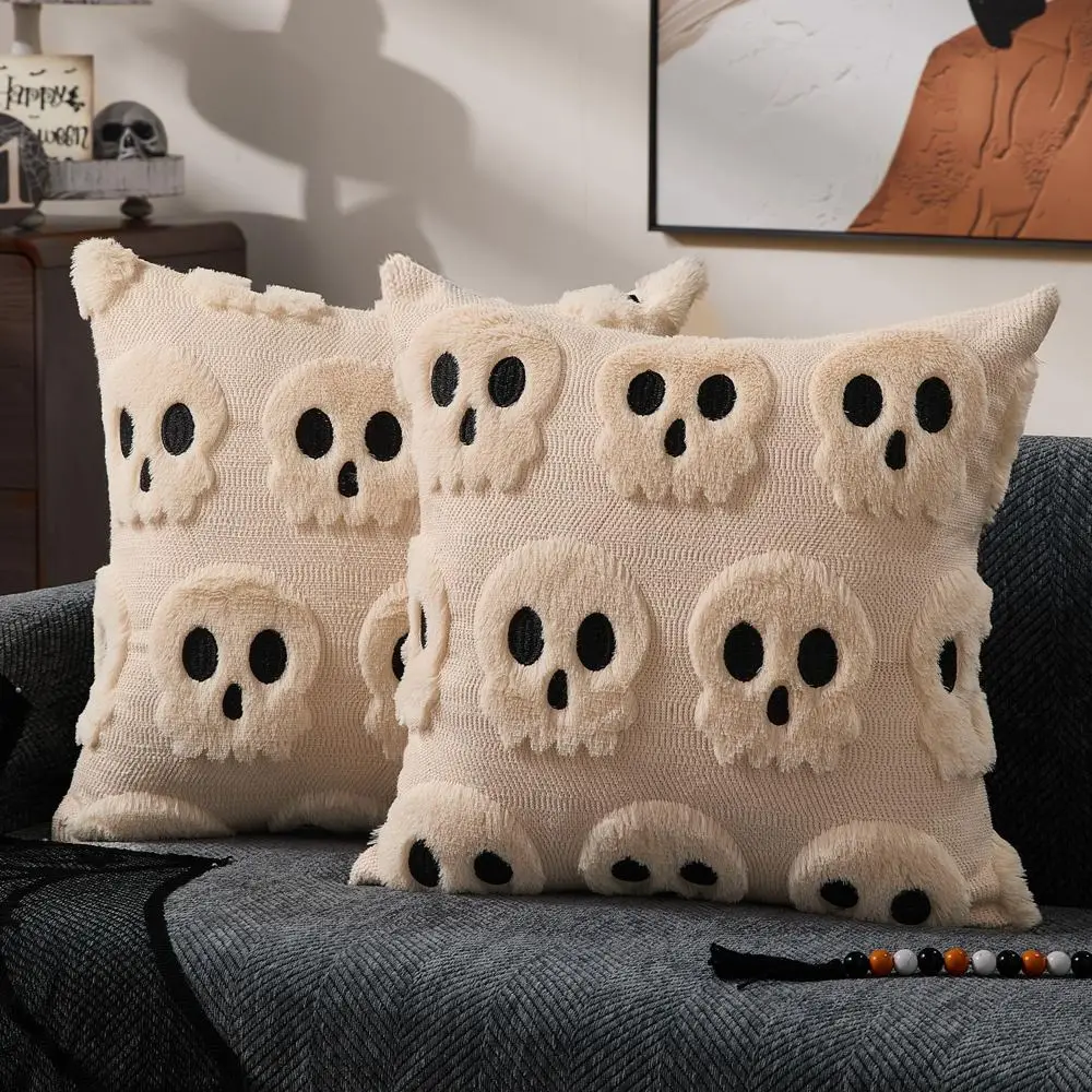 Zwei cremefarbene Kissen mit plastischen Totenkopf-Motiven auf einem dunklen Sofa