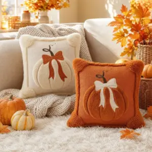 Zwei Kissenhüllen mit Kürbis und Schleife in Creme und Orange auf einem Sofa