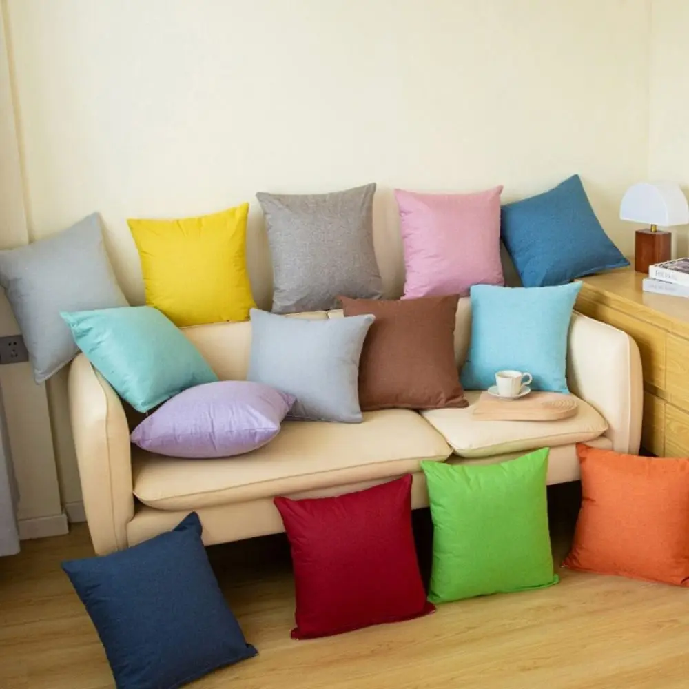Mehrere einfarbige Kissenbezüge in bunten Farben, darunter Orange, auf einem hellen Sofa und dem Boden
