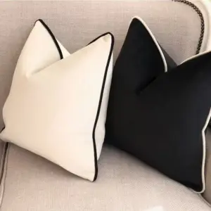 Ein cremeweißes und ein schwarzes Kissen mit Kontrastkante auf einem Sofa