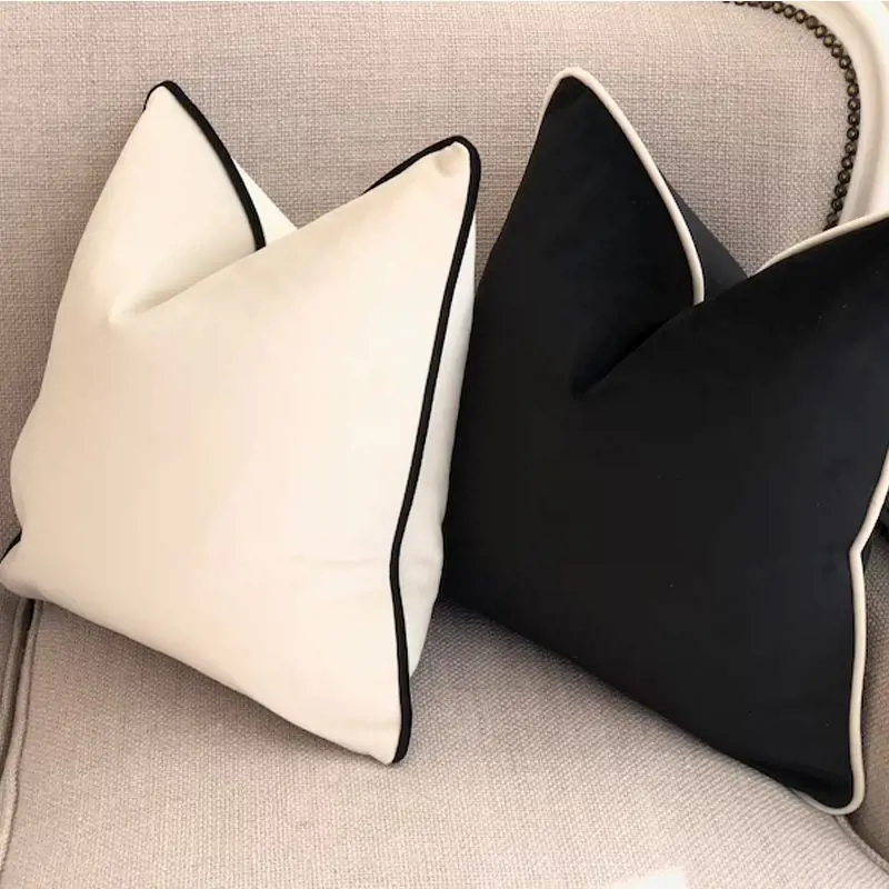 Ein cremeweißes und ein schwarzes Kissen mit Kontrastkante auf einem Sofa