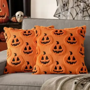 Zwei orangefarbene Kissenbezüge mit Kürbisgesichtern auf einem grauen Sofa