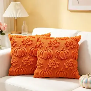 Zwei orangefarbene Kissenhüllen mit Kürbis- und Blattmuster auf einem hellen Sofa