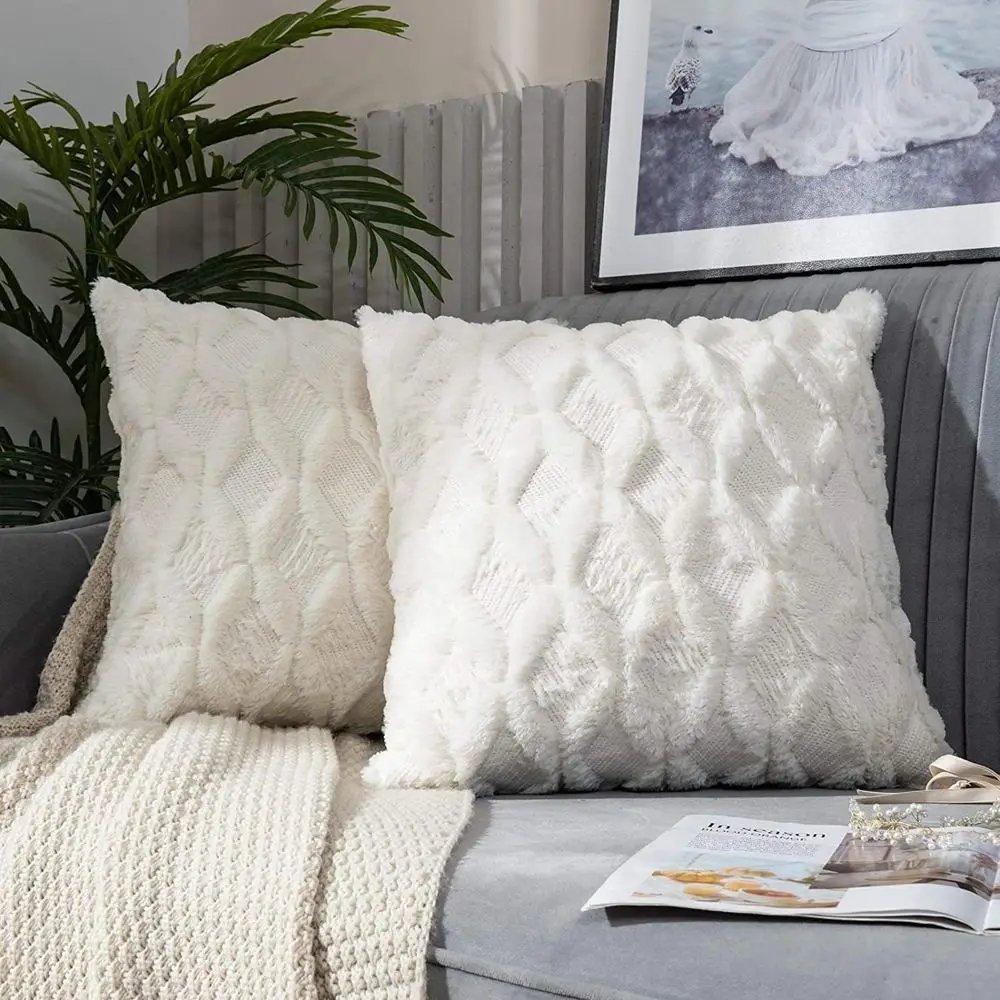 Zwei cremeweiße Kissenhüllen mit Rautenmuster in flauschiger Optik auf einem Sofa mit Decke