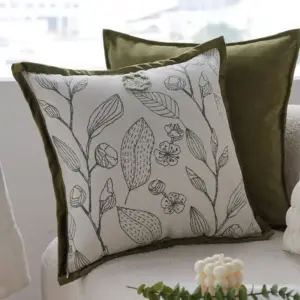 Kissenbezug mit grauem Pflanzenmuster und olivgrüner Einfassung vor einem Sofa