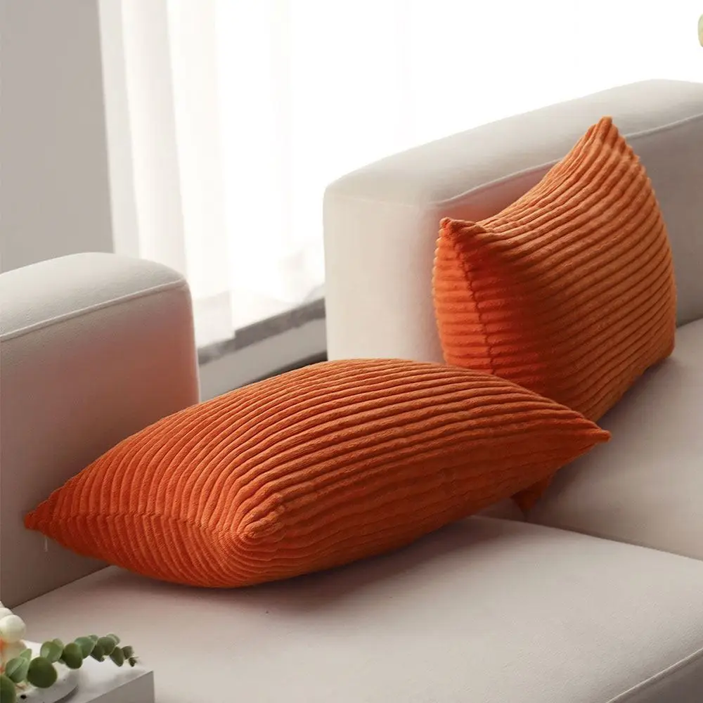 Zwei orange Kissenbezüge mit Querrippen auf einem hellen Sofa