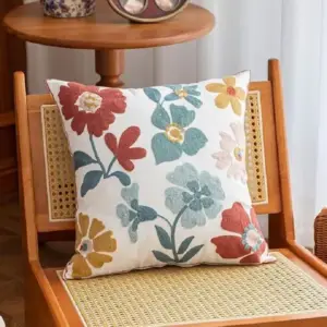 Kissenhülle mit bunten gestickten Blumen auf einem Rattanstuhl