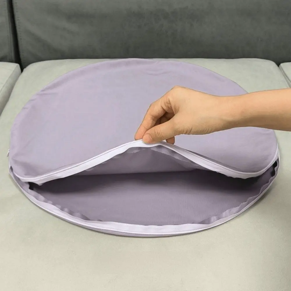 Runder lila Kissenbezug mit geöffnetem Reißverschluss auf einem Sofa