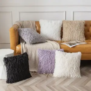 Mehrere zottelige Kissen in Grau, Schwarz, Lila und Creme auf einem Ledersofa