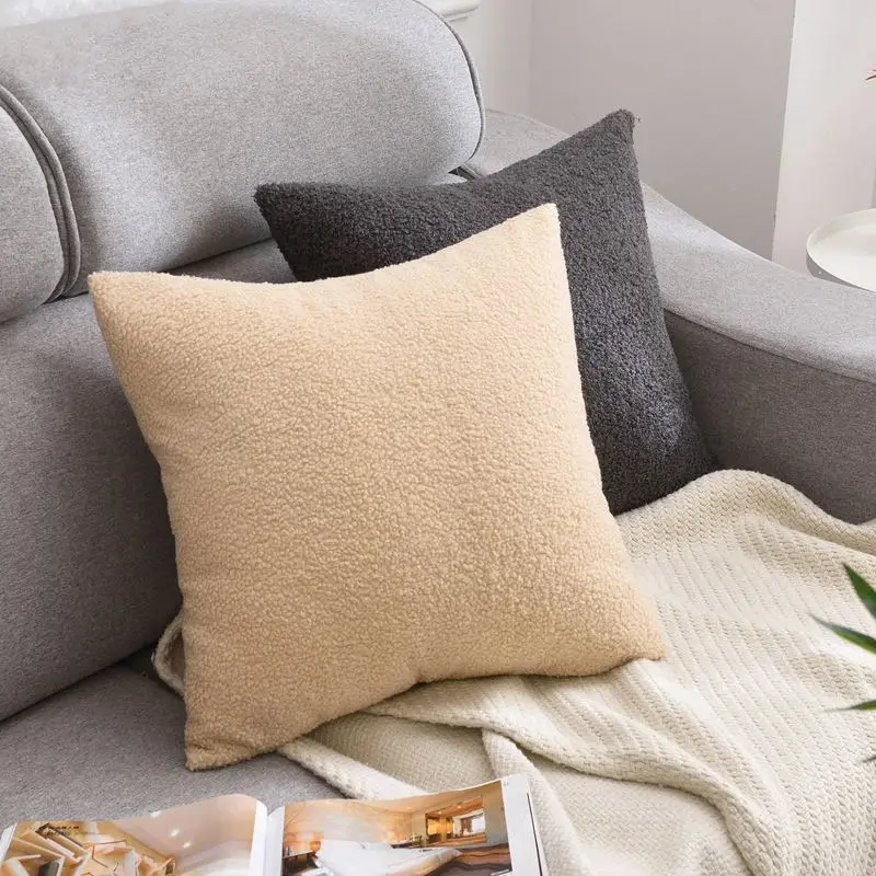 Beigefarbenes Kissen mit weicher Teddy-Struktur vor einem grauen Sofa