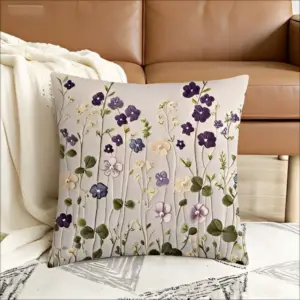 Graues Kissen mit lila und cremefarbenen Wildblumen in Stickerei-Optik vor einem braunen Sofa