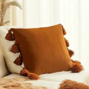 Rostbrauner Kissenbezug mit Quasten an den Rändern auf einem hellen Sofa
